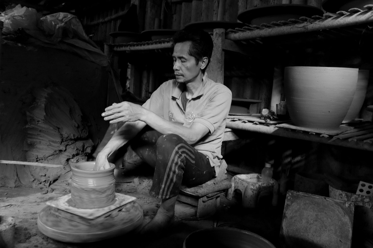 wide shot of an okinawan artist in a studio with a large canvas and tools