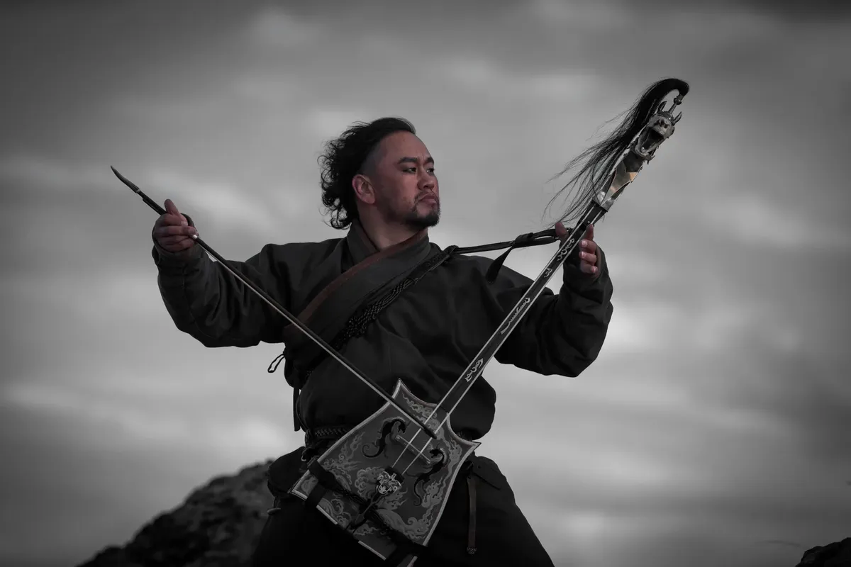 Traditional musician playing a morin khuur outdoors, showcasing cultural heritage and the art of music in nature.
